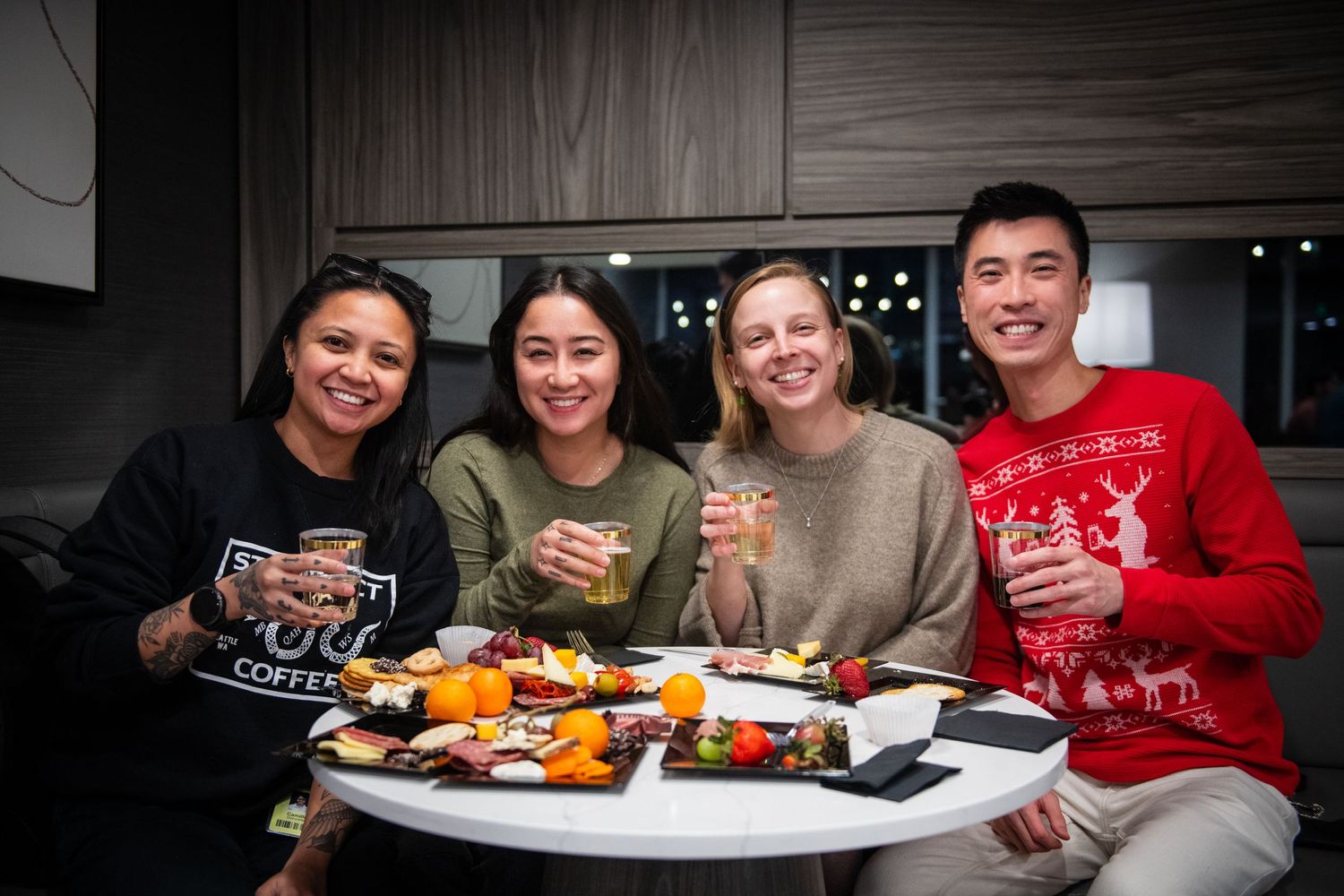 Friends enjoying appetizers and drinks while wearing festive holiday sweaters.