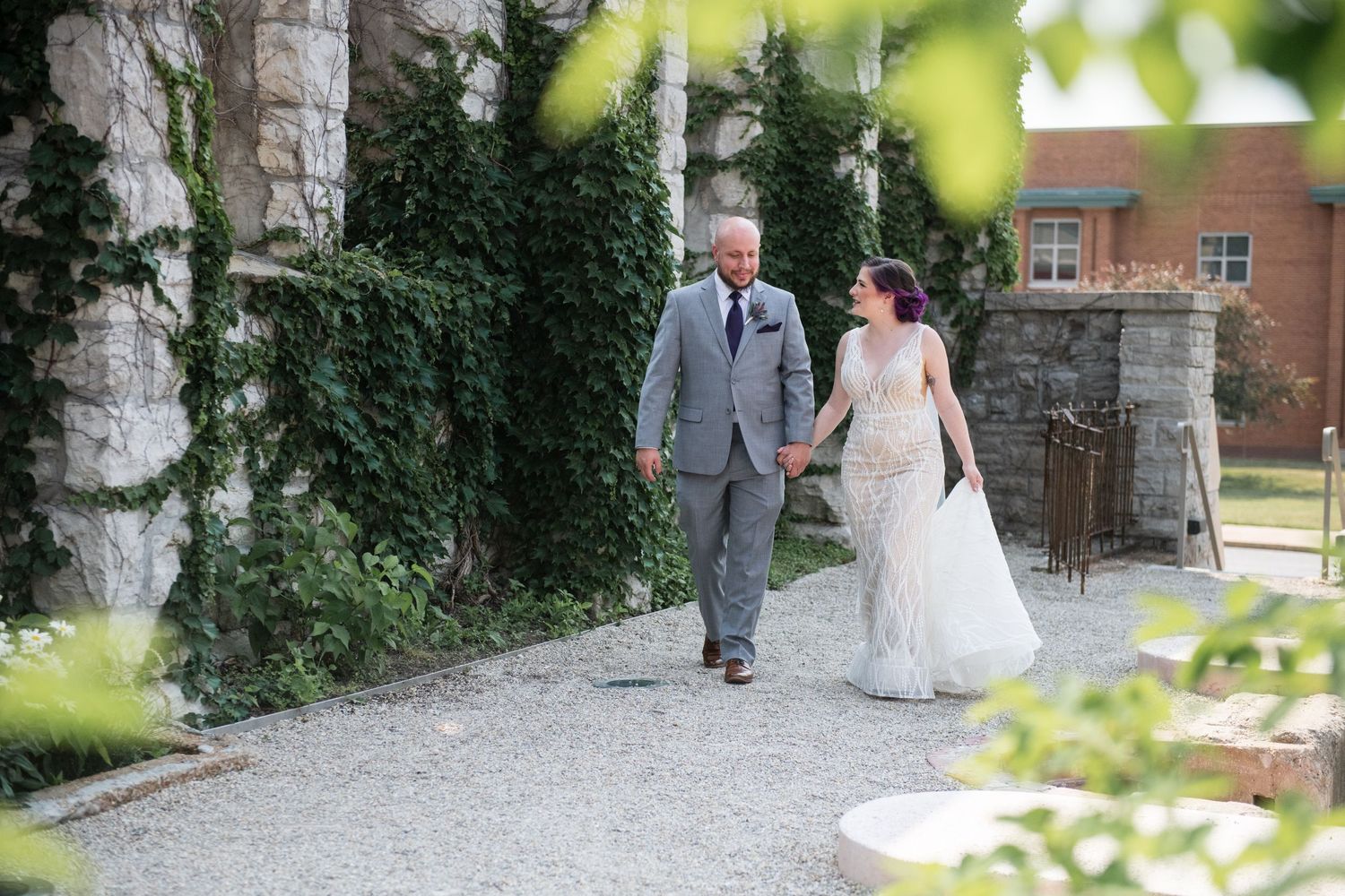 Couple walks along a garden path in wedding attire.