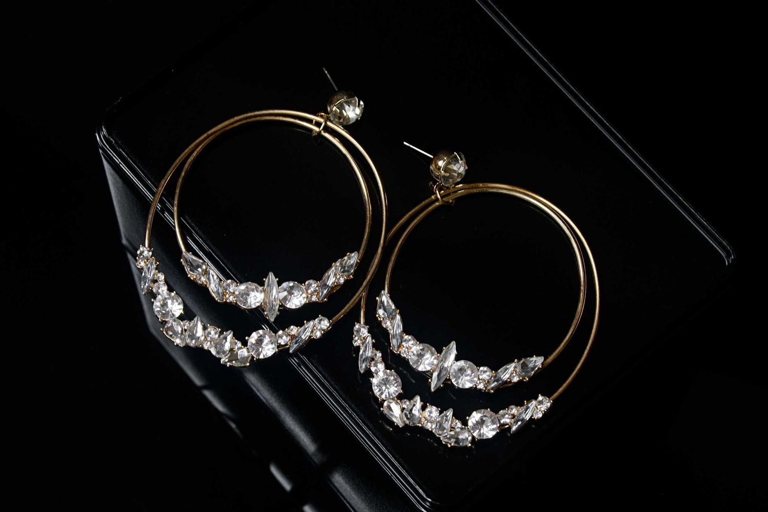 Gold hoop earrings adorned with delicate crystal embellishments against a dark background.