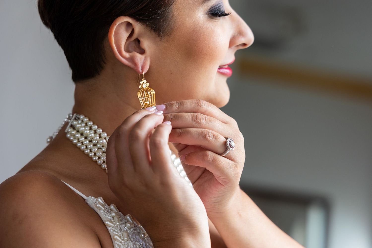 Close-up of pearl necklace and gold earring being put on for wedding day.