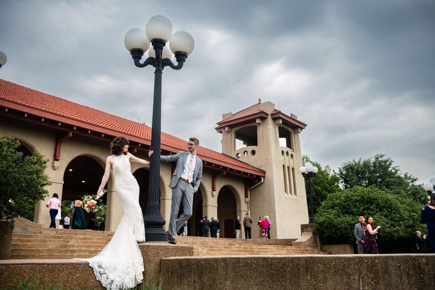 Wedding couple posing outside Spanish-style building with bell tower and lamp post.