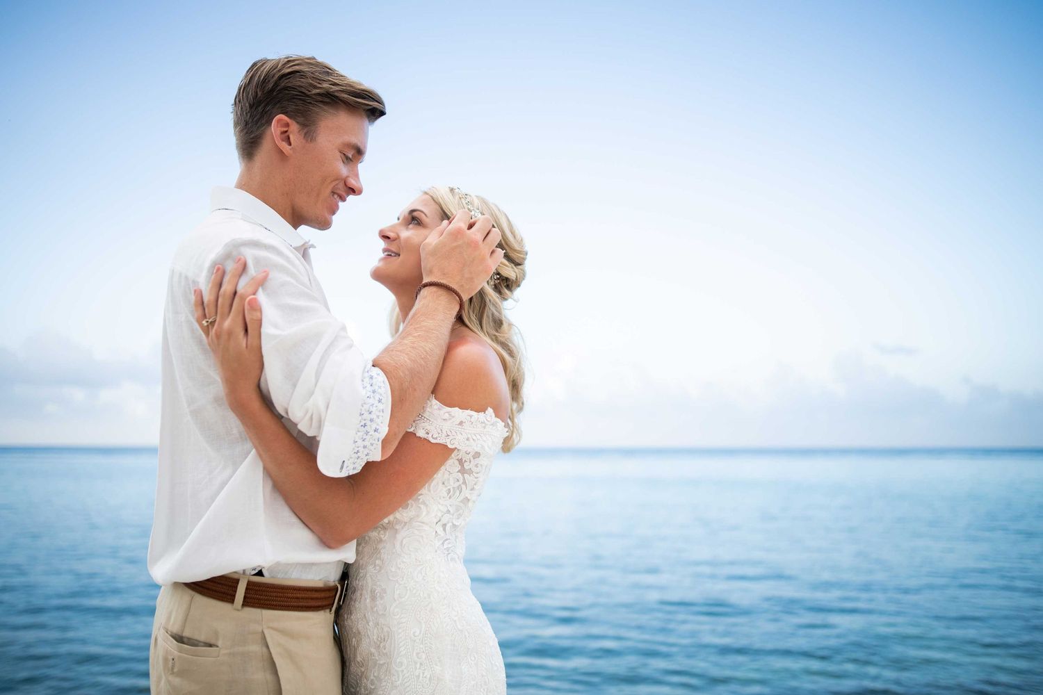 Romantic couple embracing on beach with ocean and blue sky backdrop.