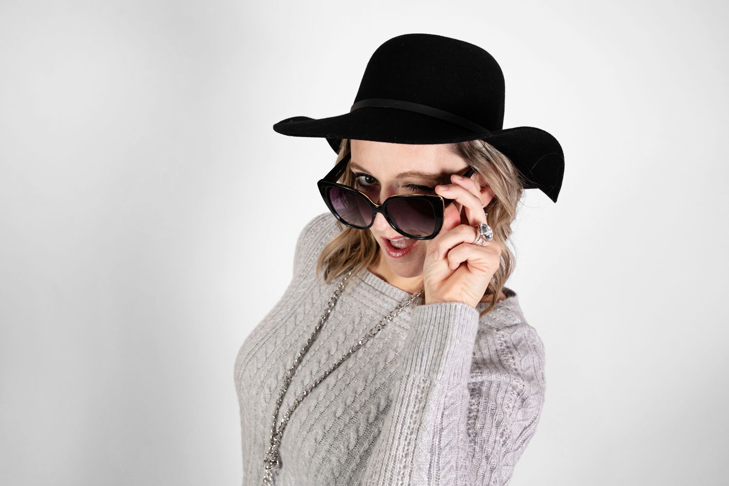 Trendy look with black hat, sunglasses and grey sweater in studio setting.