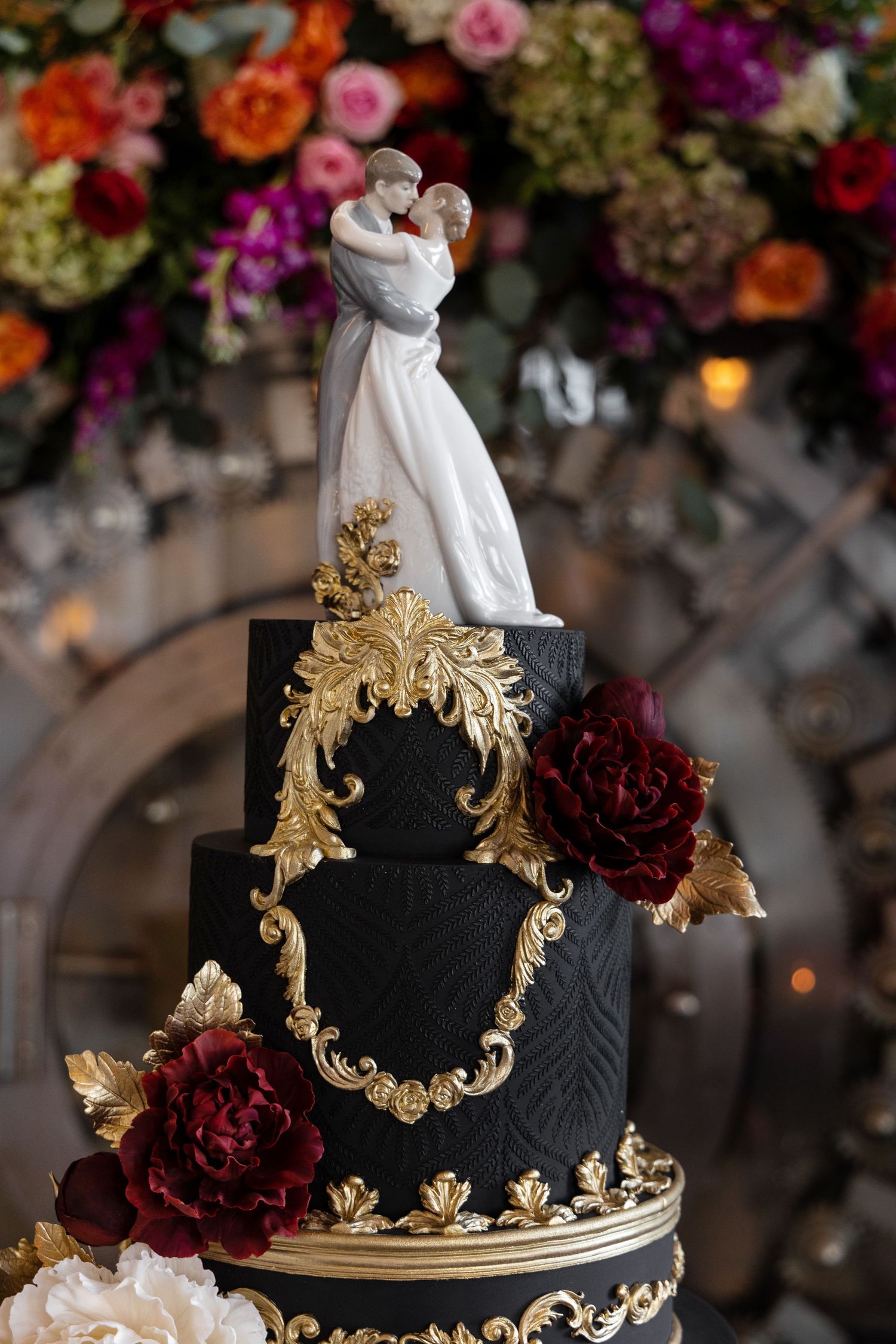 Dramatic black and gold wedding cake with ornate baroque details and deep red roses.