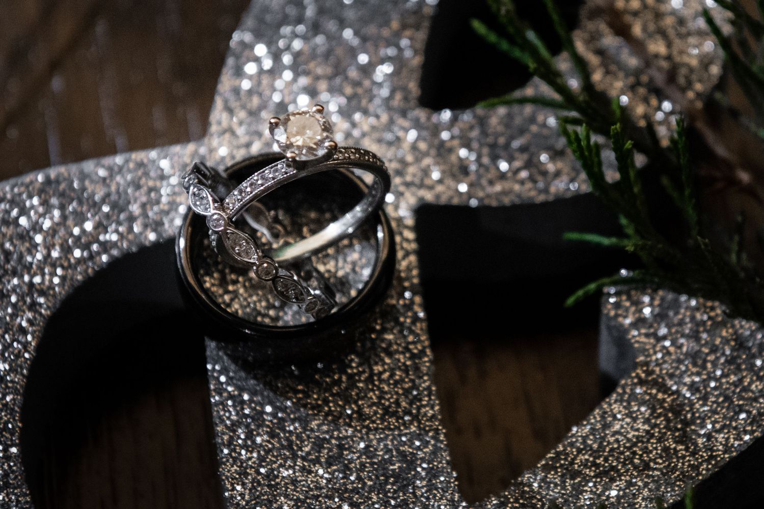 Close-up of wedding rings on sparkly silver ribbon with dark wooden background.