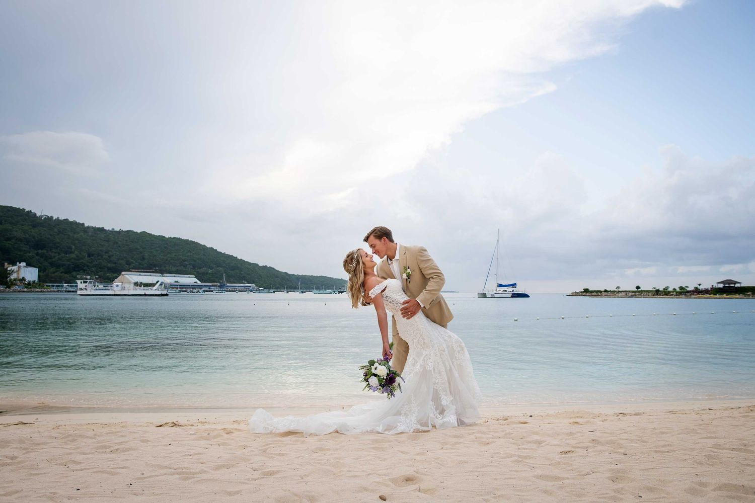 A romantic beachside wedding ceremony with turquoise waters, white sand, and soft clouds in the distance.