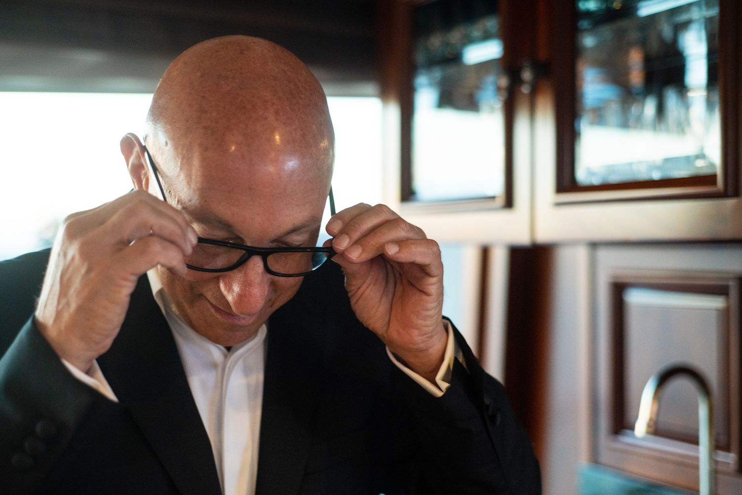 Person in formal attire adjusting glasses indoors.
