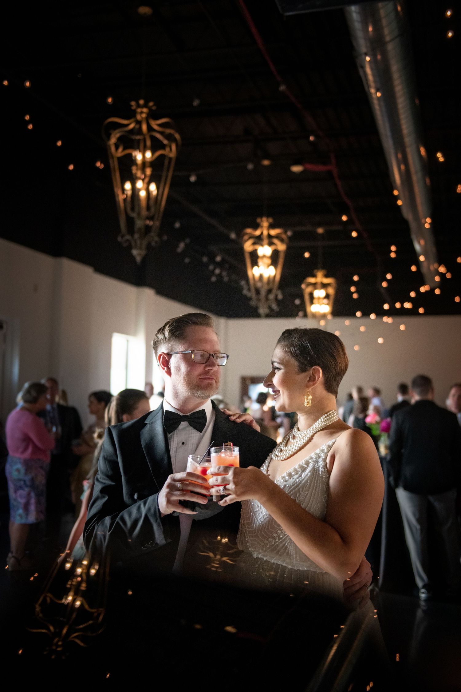A formal event scene with guests enjoying cocktails under elegant hanging lanterns in a dark venue.