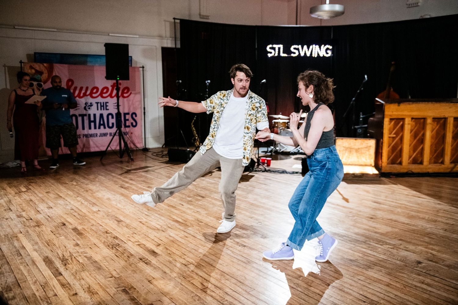 Dancers perform energetic swing moves on a wooden dance floor at STL Swing studio.