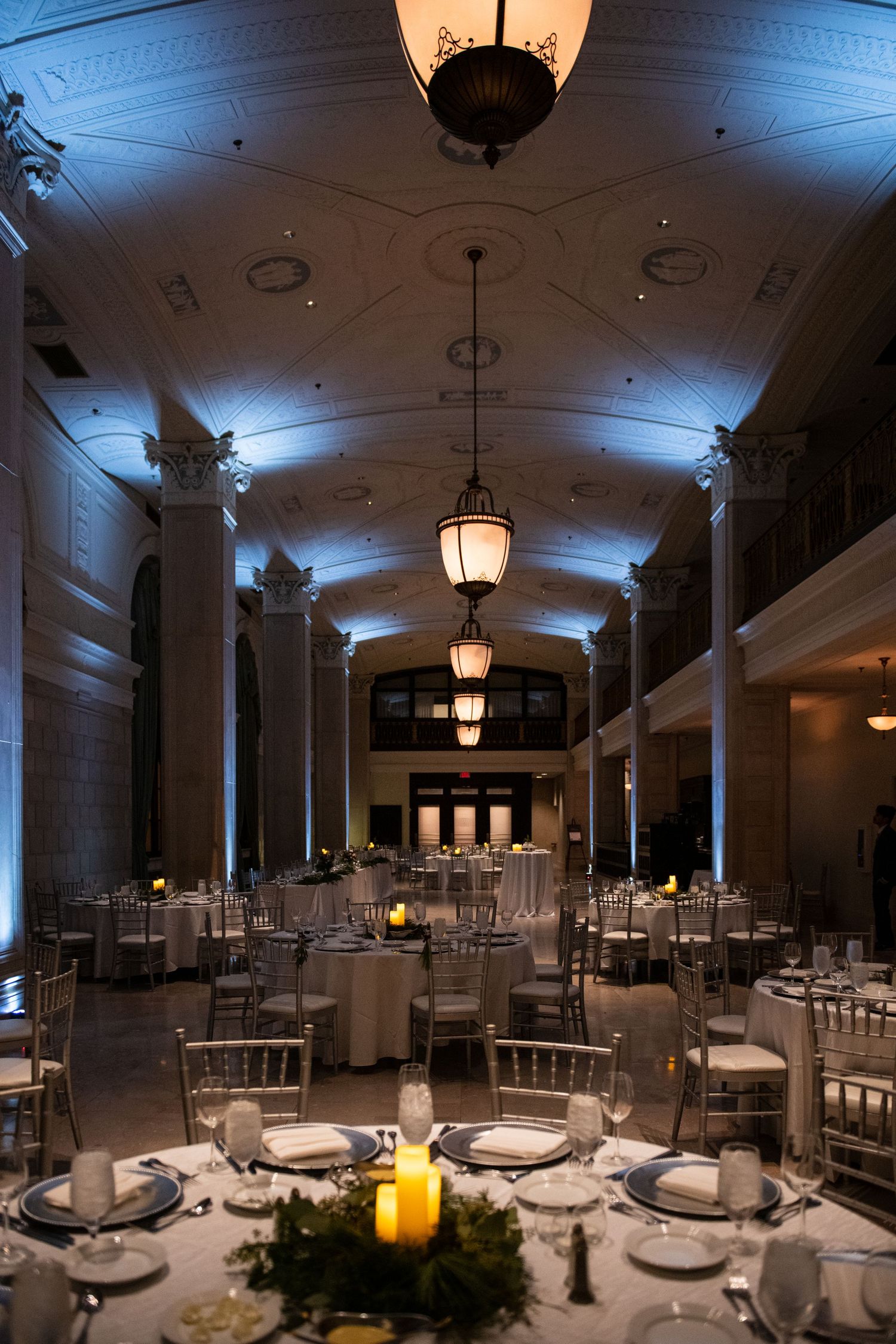 Majestic columned hall with vaulted ceilings and round dining tables illuminated by vintage pendant lights.