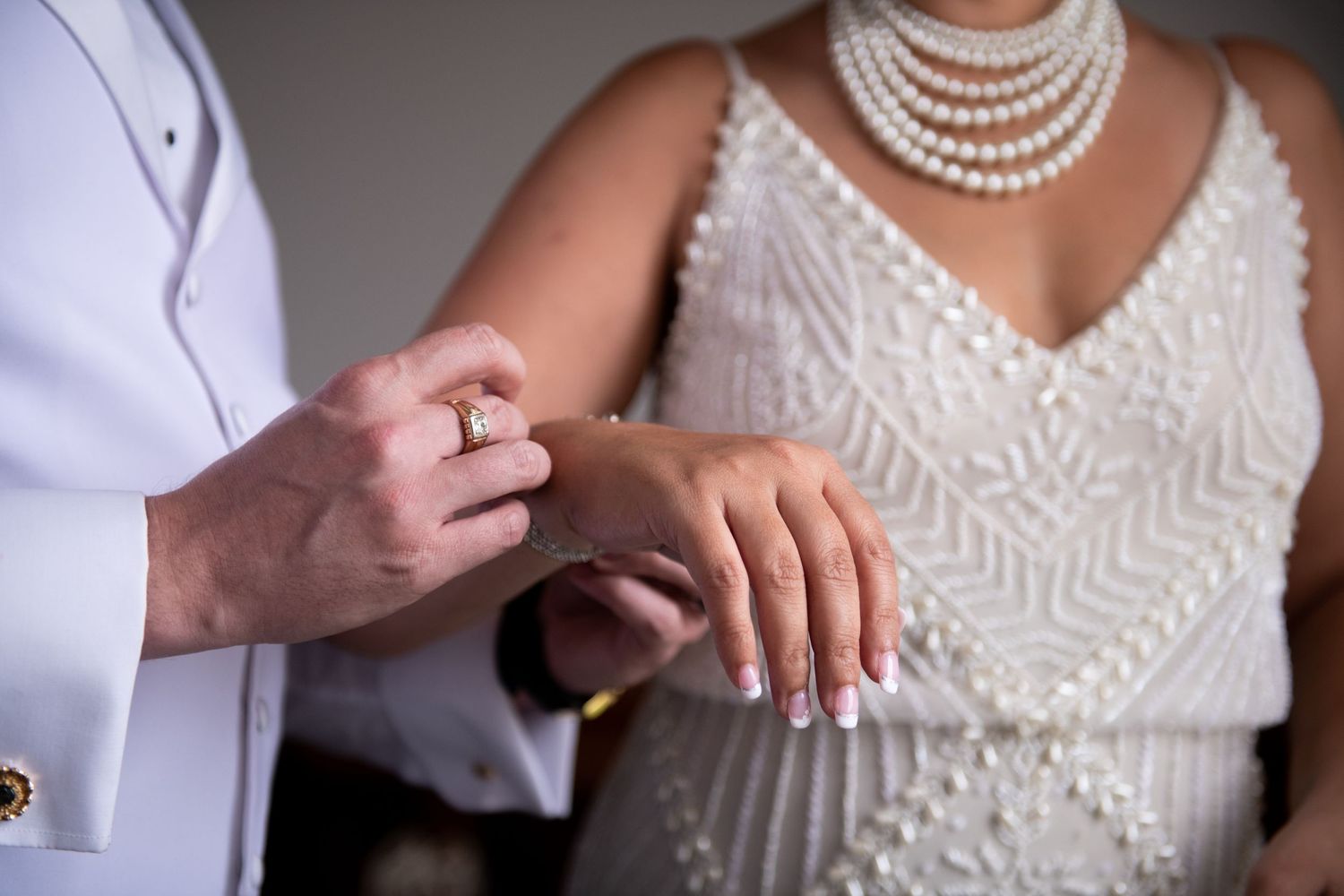 Detail shot of hands exchanging rings with white formal attire and pearl necklace.
