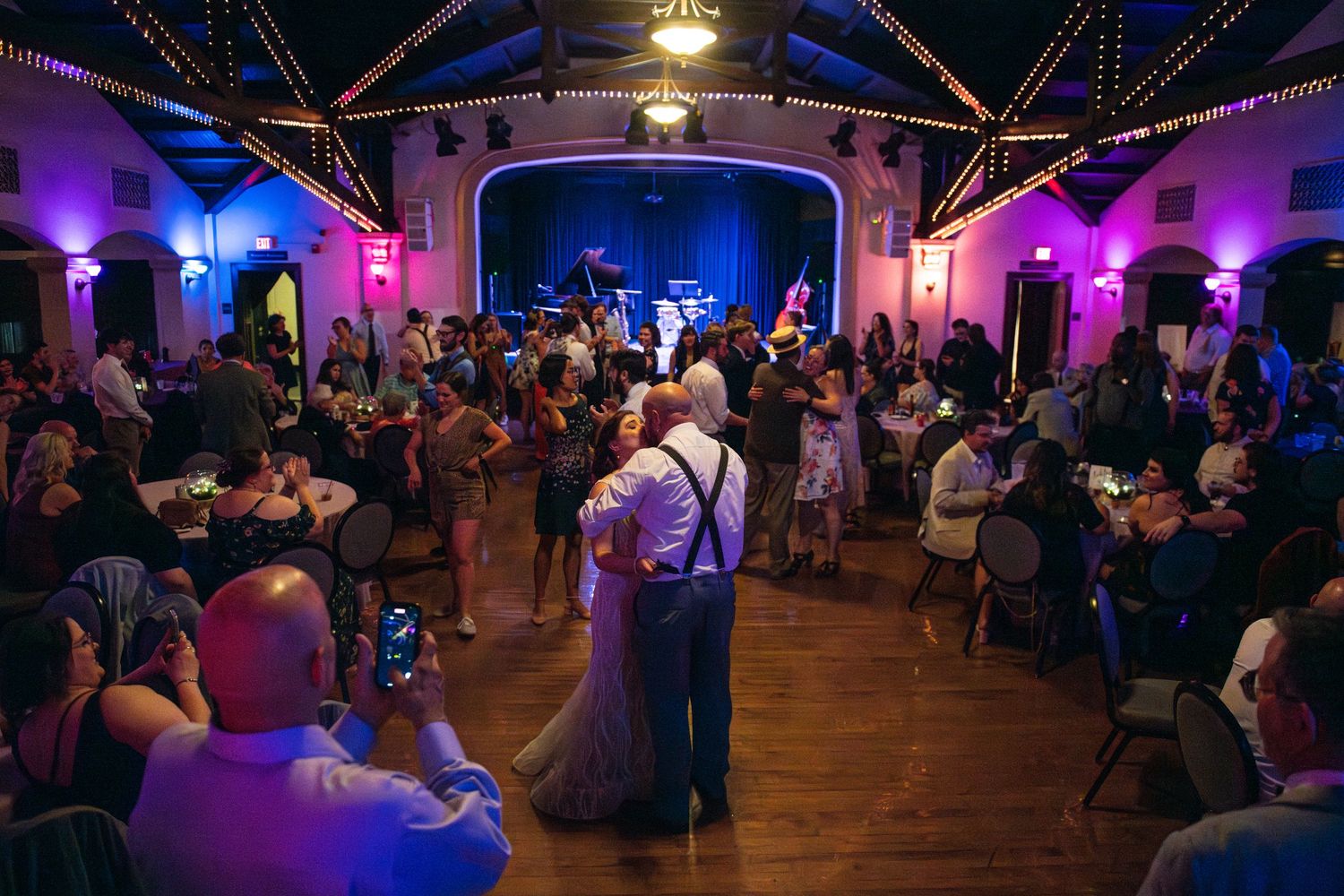 Wedding reception venue with colorful mood lighting and guests dancing on a wooden dance floor.