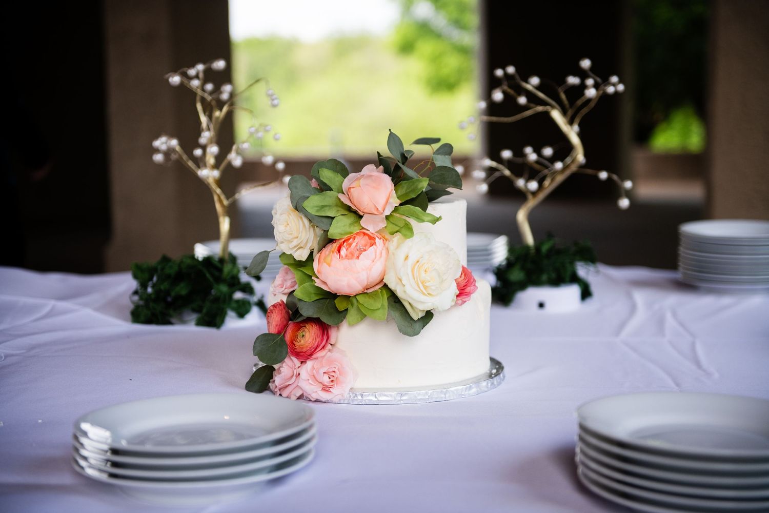 Elegant white wedding cake decorated with fresh pink roses and baby's breath on a white tablecloth.