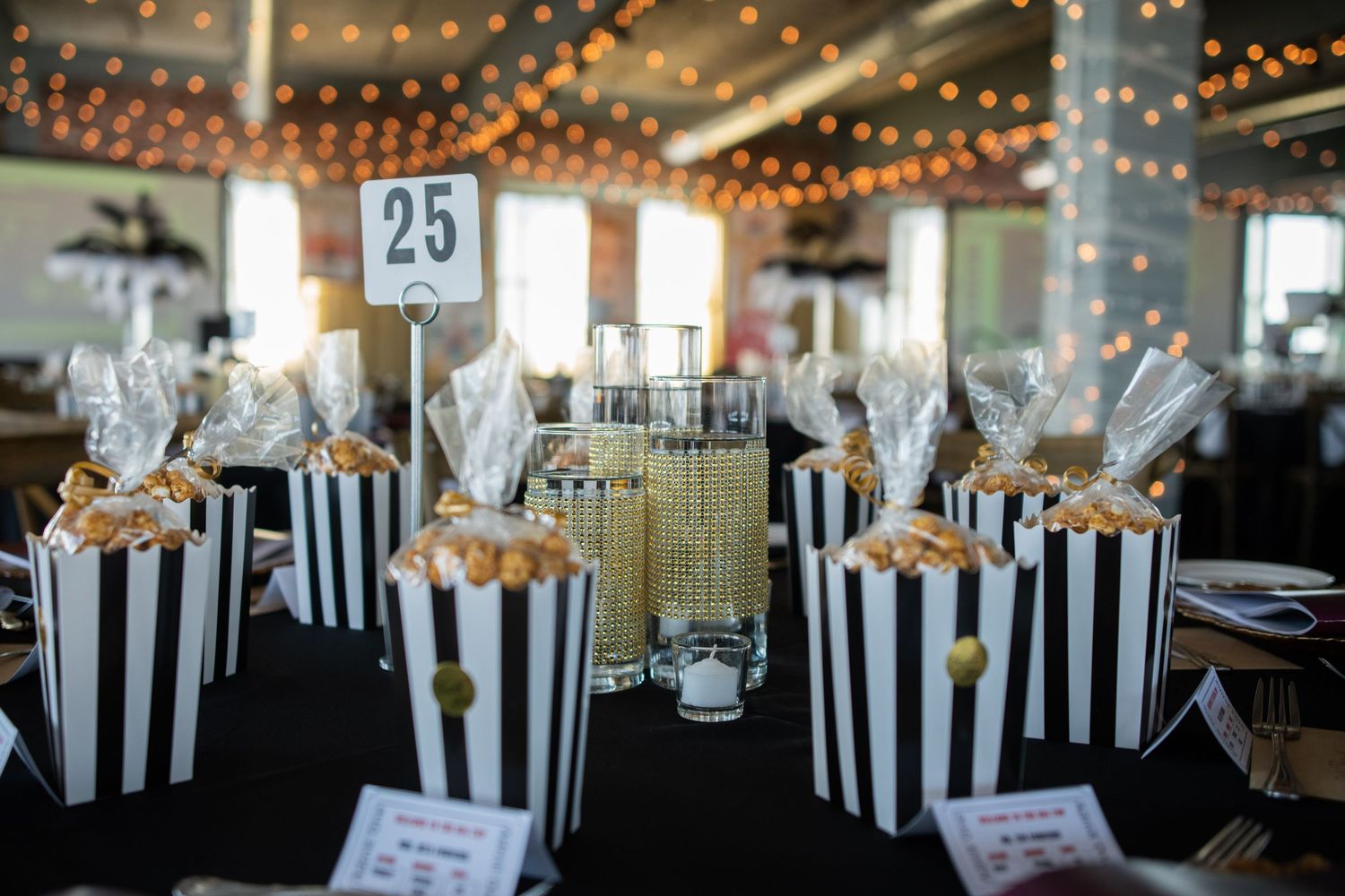 Black and white striped popcorn boxes arranged as table decorations with string lights overhead.
