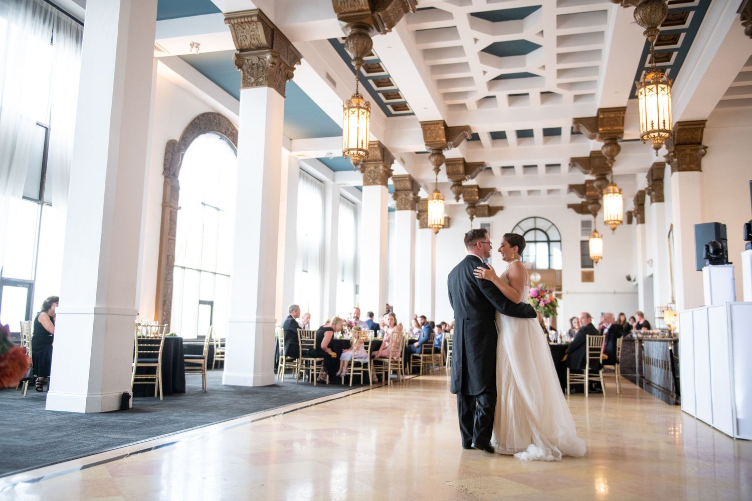 Couple sharing dance in grand ballroom with ornate architectural details and hanging lanterns.