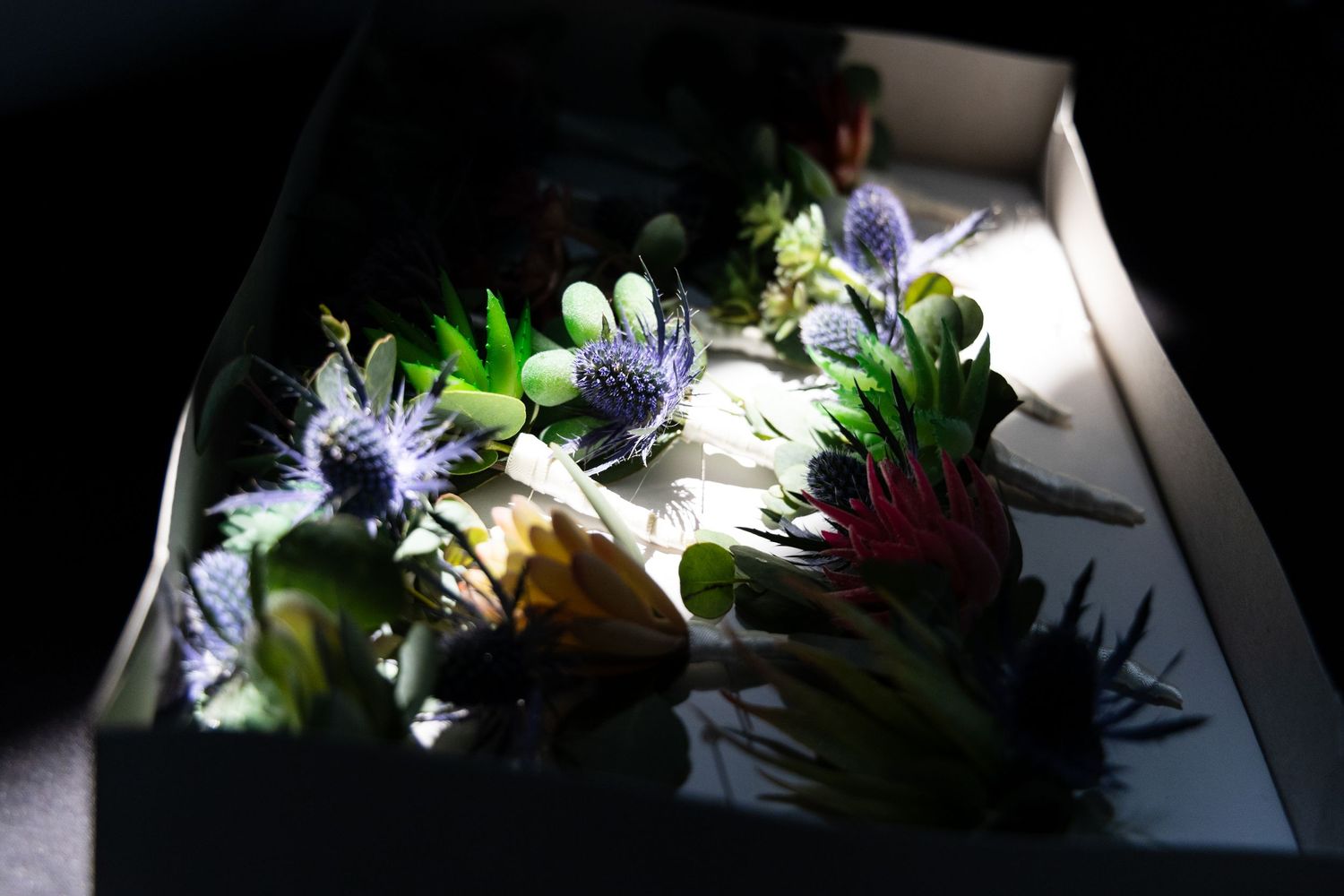 Artistically lit box of fresh sushi and sashimi with purple flowers and garnishes.