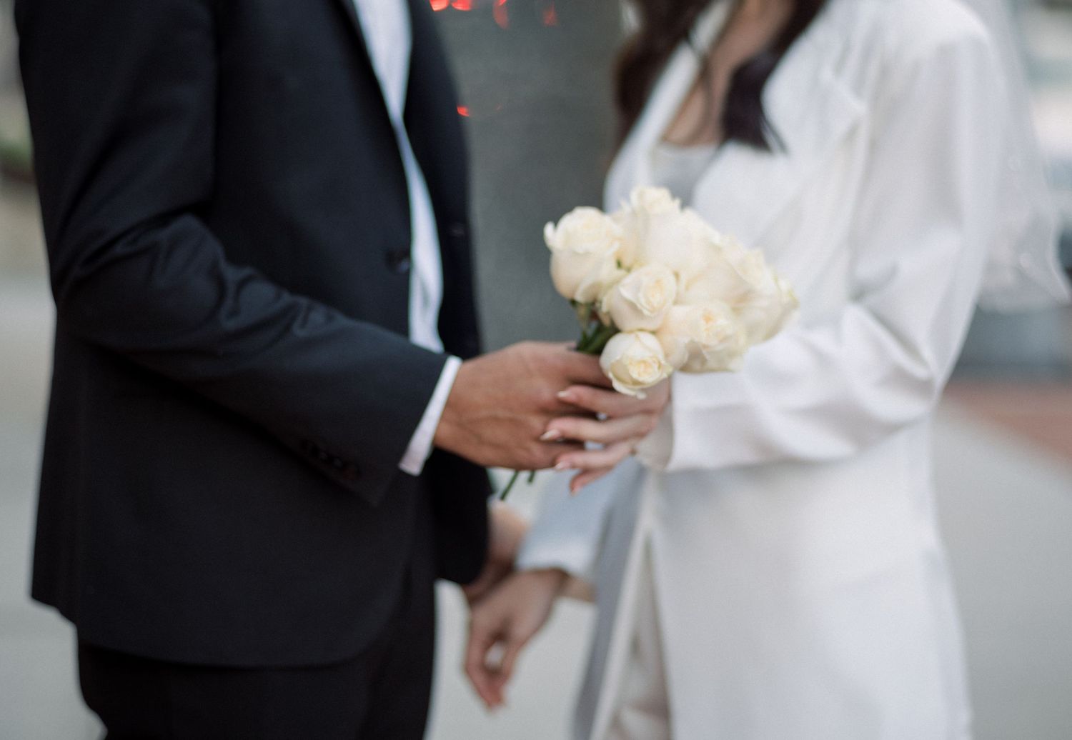 A couple sharing a moment while holding white roses against formal attire.