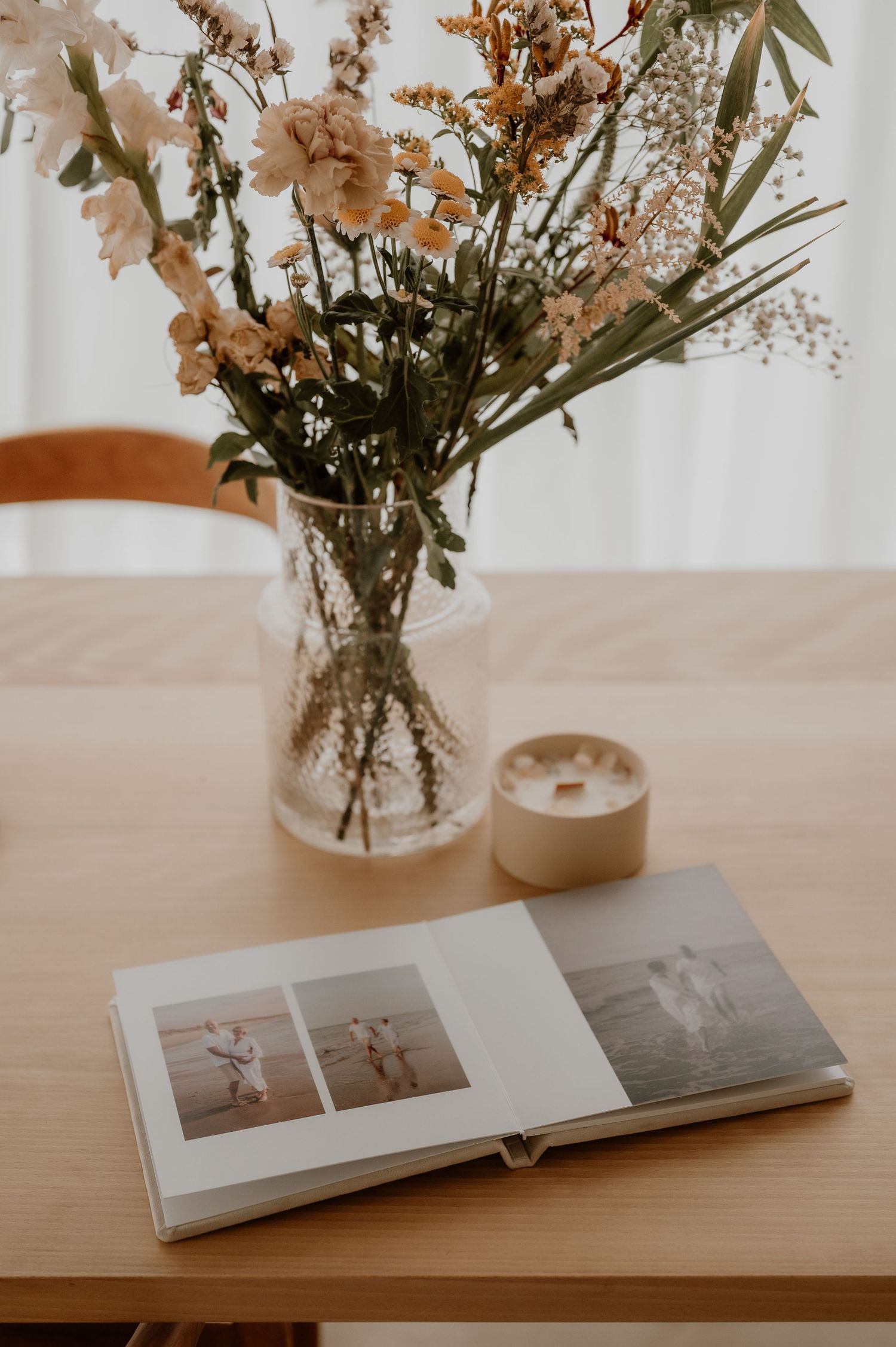Bloemstuk in een glazen vaas naast een open fotoalbum op een houten tafel, vastgelegd in zacht natuurlijk licht.