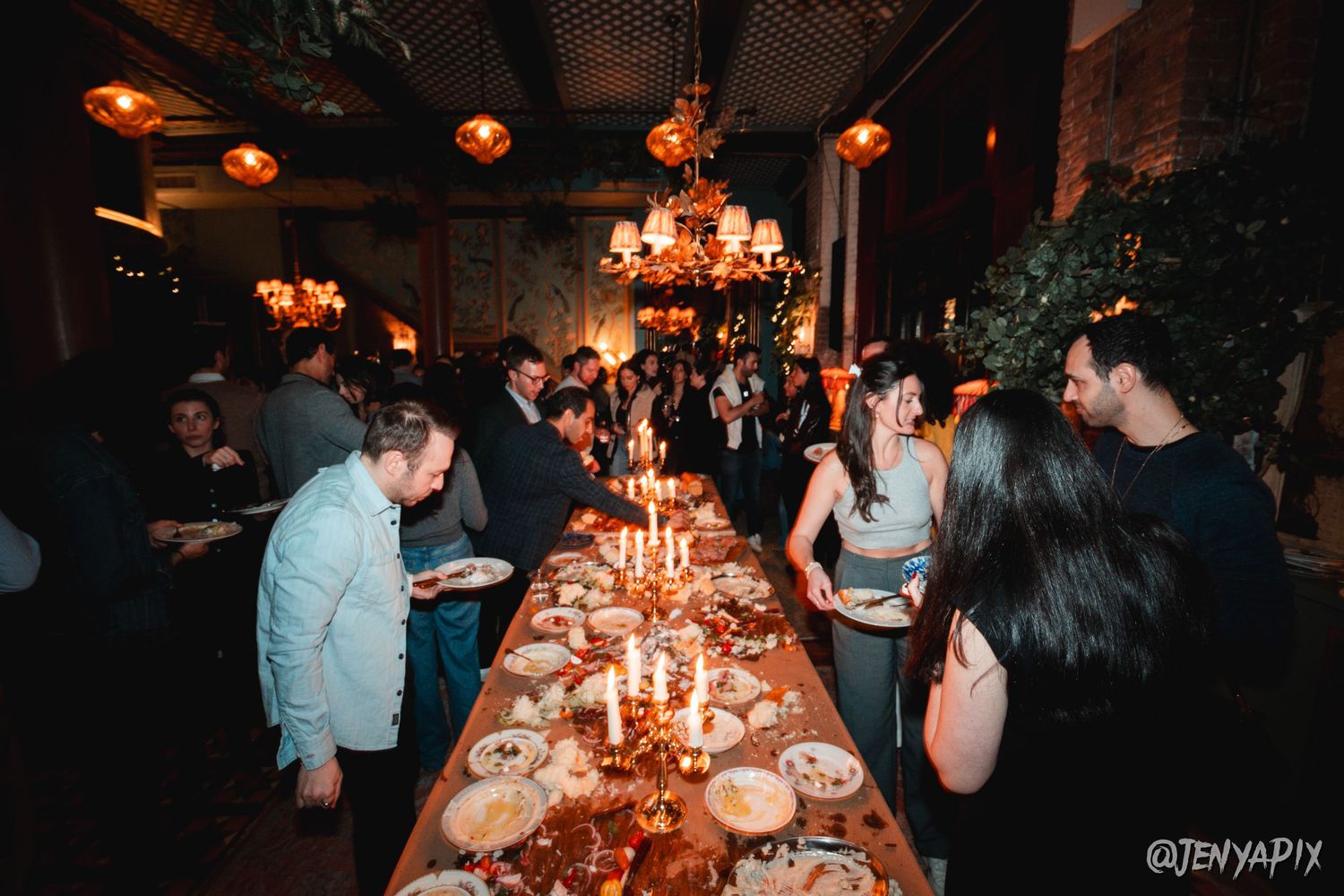 People enjoying a social gathering around a long table adorned with candles and chandeliers overhead.