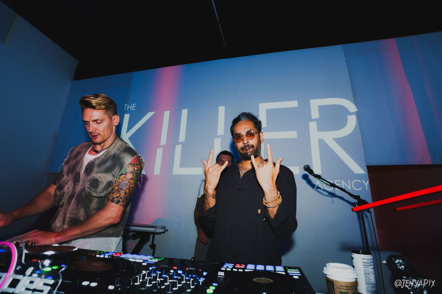 DJs performing on stage with equipment under blue and red lighting effects.