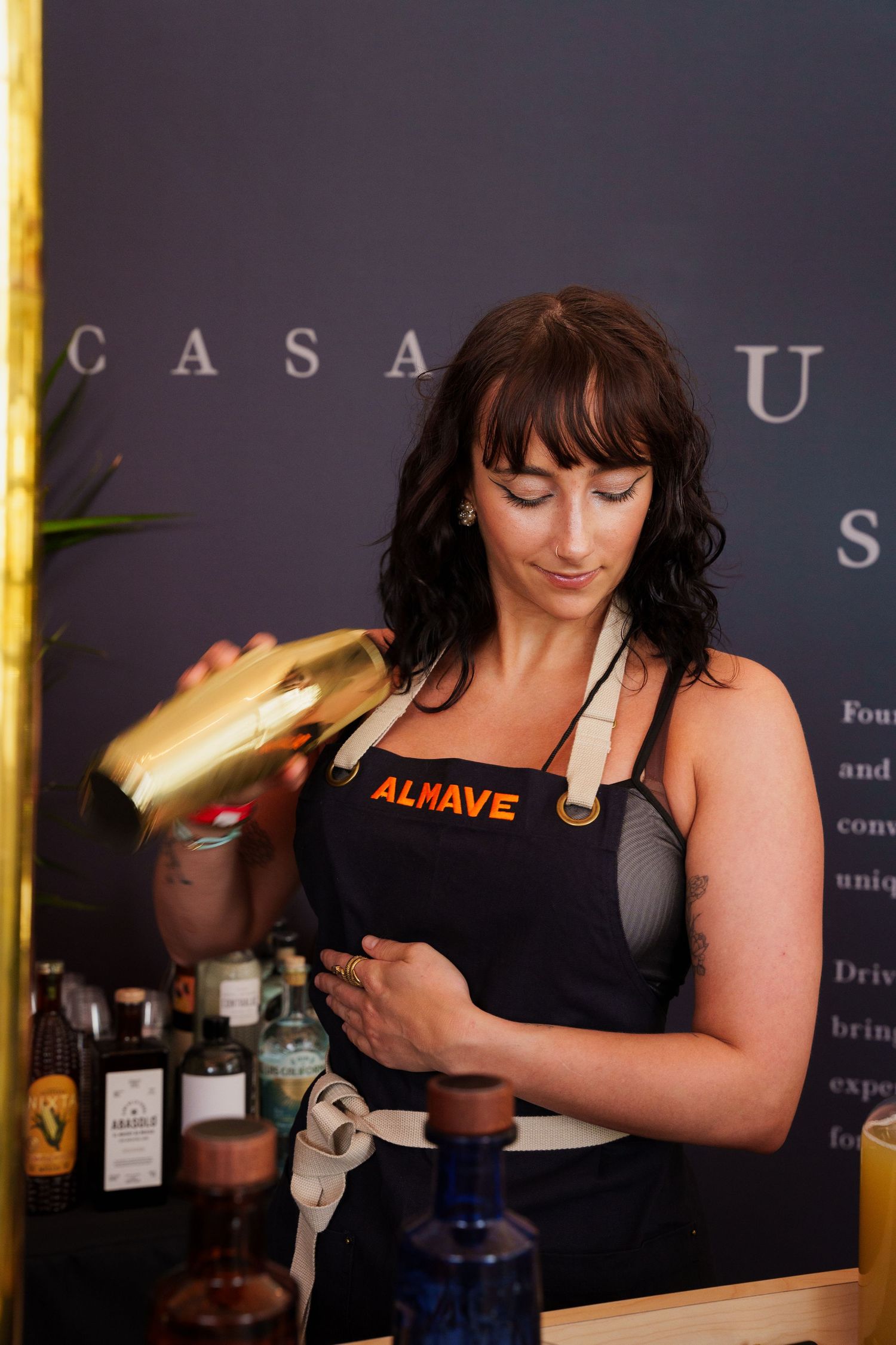 A bartender in a black Almave apron pours a drink behind the bar.