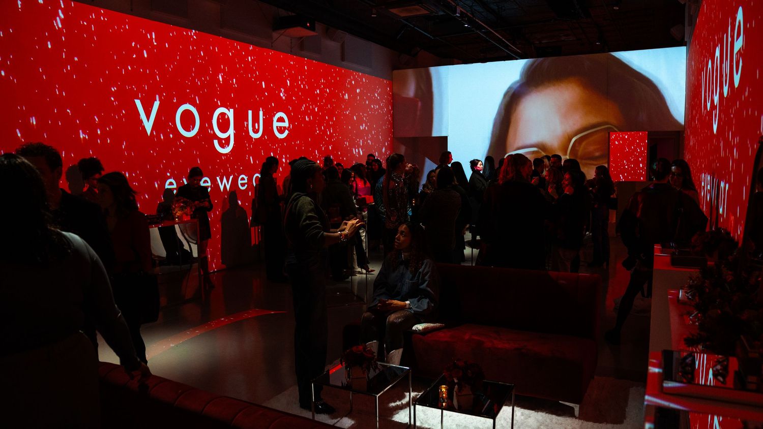 Red-lit event space with Vogue branding and silhouetted crowd gathering.