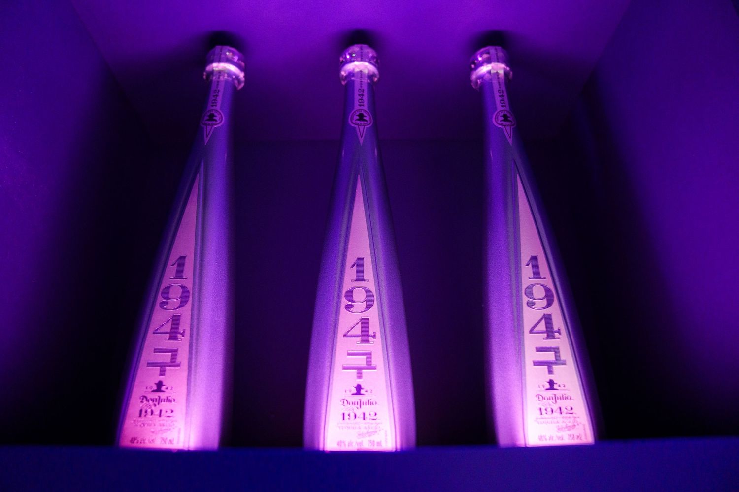 Three illuminated Don Julio tequila bottles glowing in purple light.