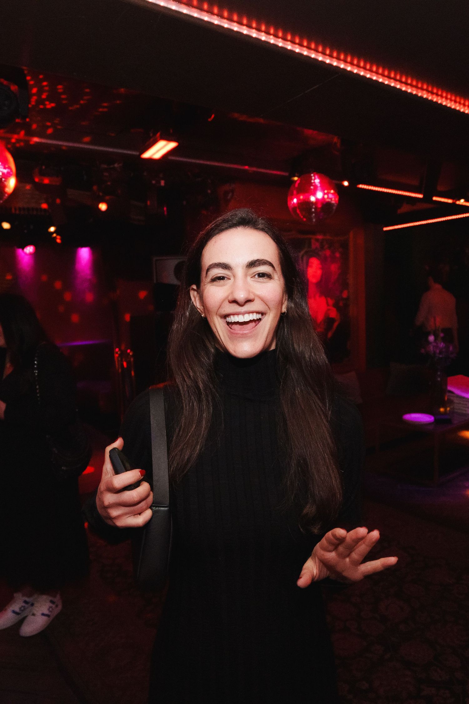 Person in black turtleneck at nightclub with pink and red lighting.