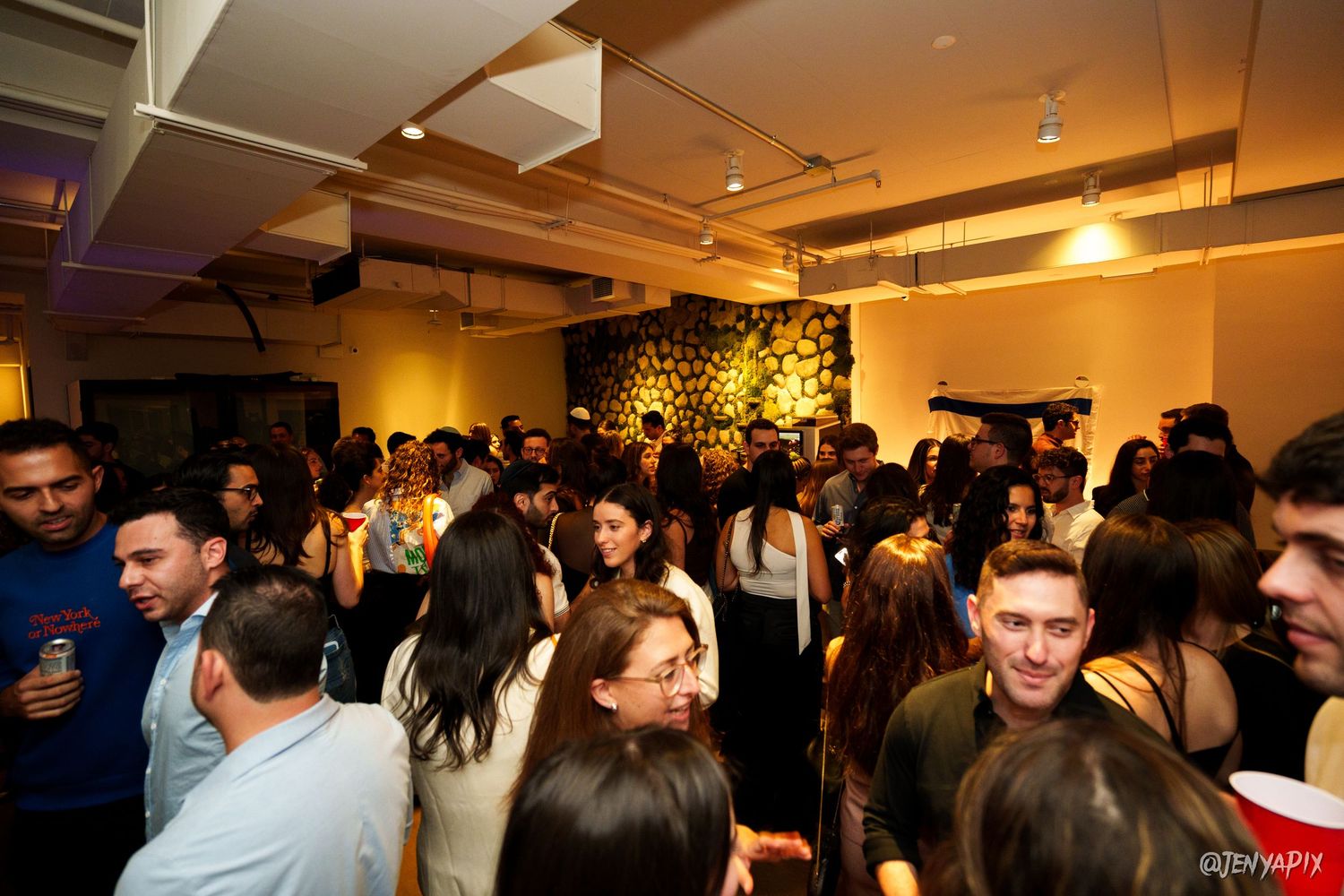 Large crowd socializing at an evening event in a modern venue with warm lighting.