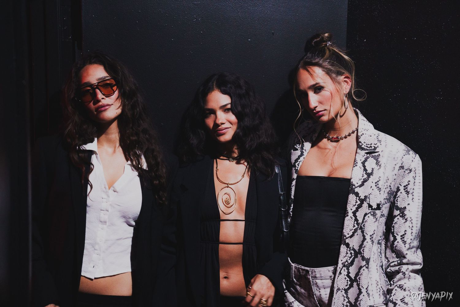Three stylish guests pose in trendy outfits at a nightclub event.