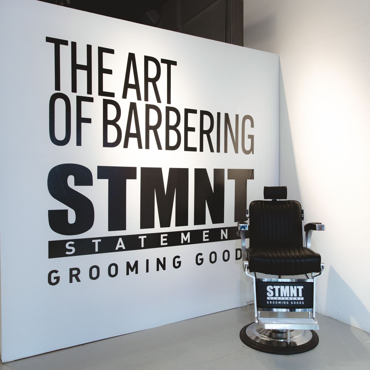Barber chair setup with STMNT grooming brand logo display featuring The Art of Barbering text.