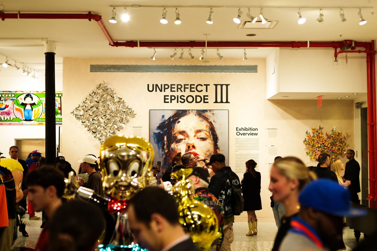 Art gallery exhibition space with large wall mural and crowd of visitors.
