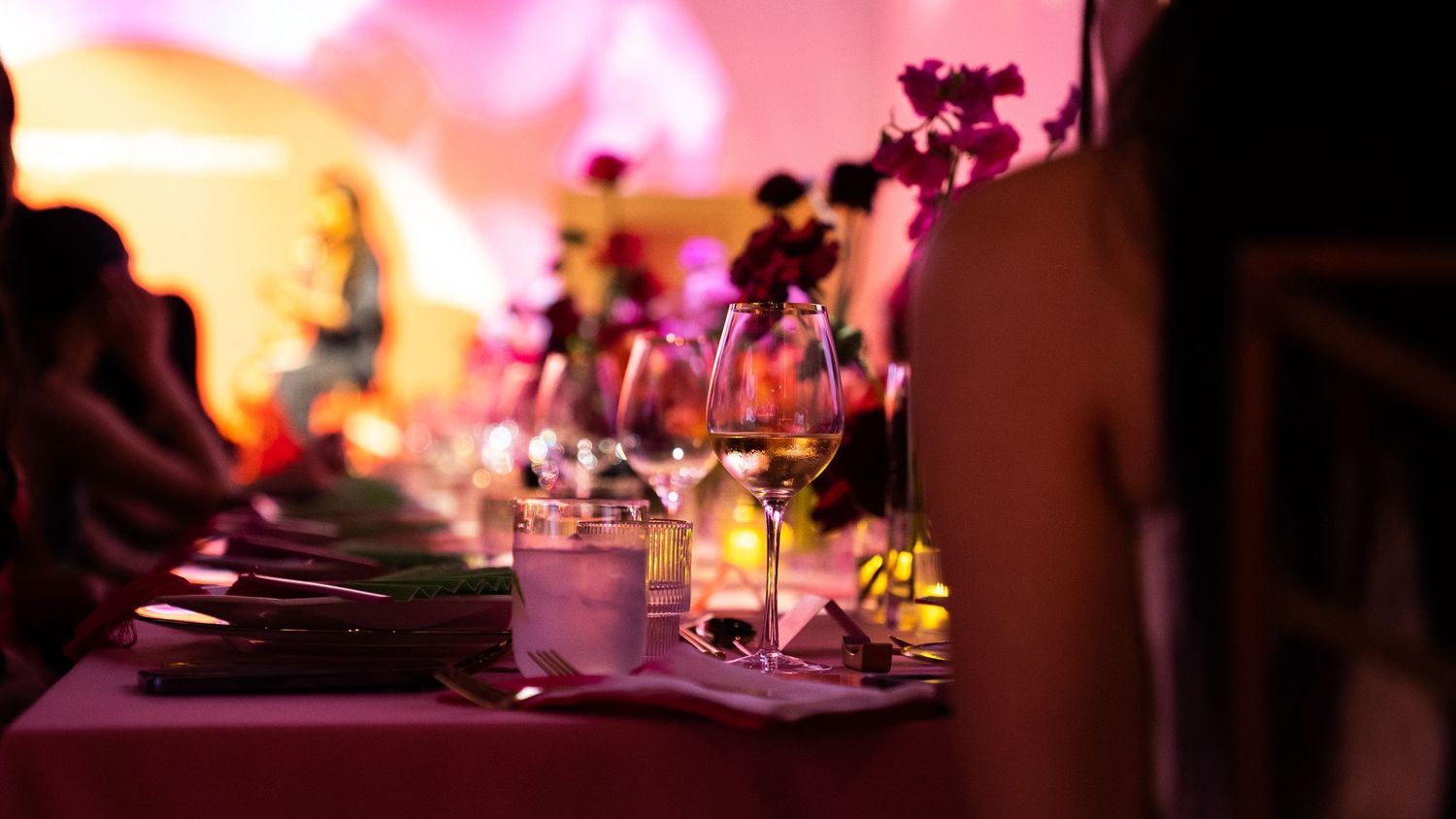 Romantic dinner table setting with wine glasses and candles under warm ambient lighting.