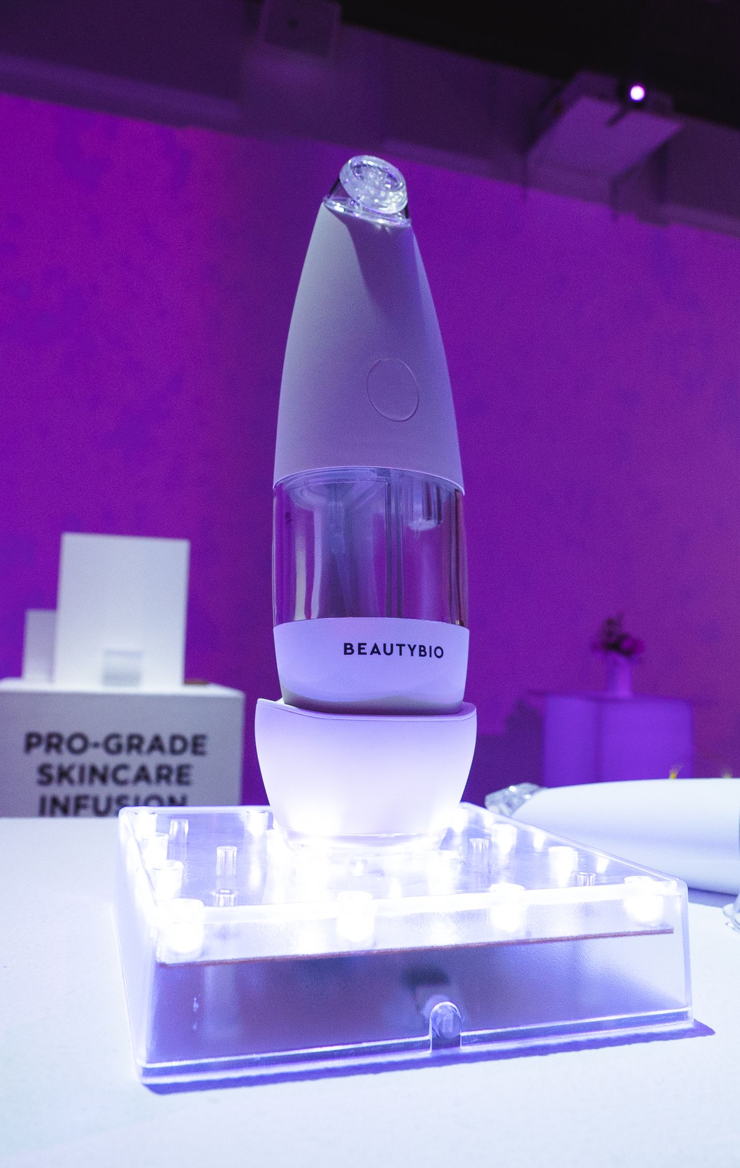 A white Beautybio skincare device displayed on an illuminated stand with purple ambient lighting.
