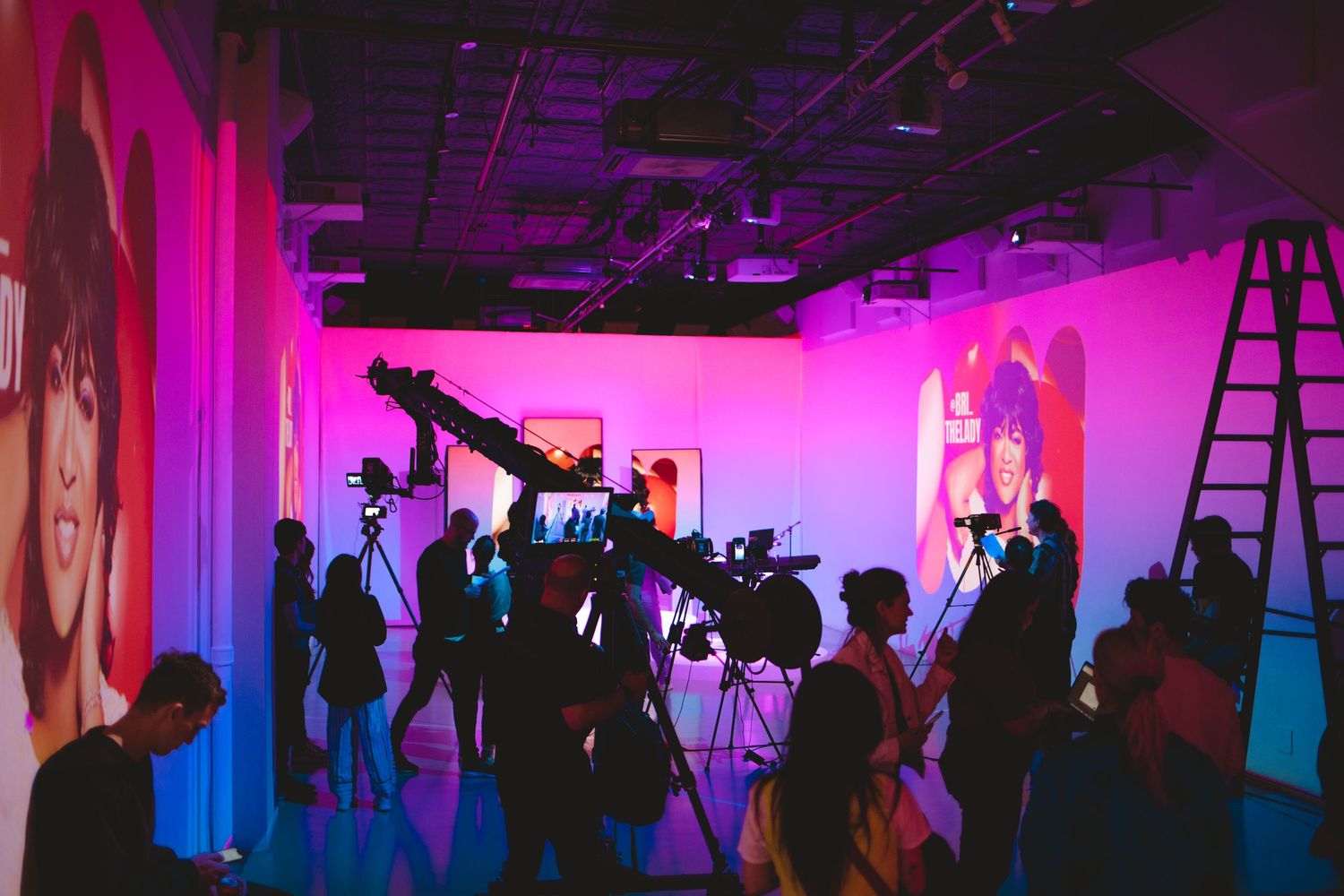 Film crew and audience silhouettes in pink-lit studio during production.