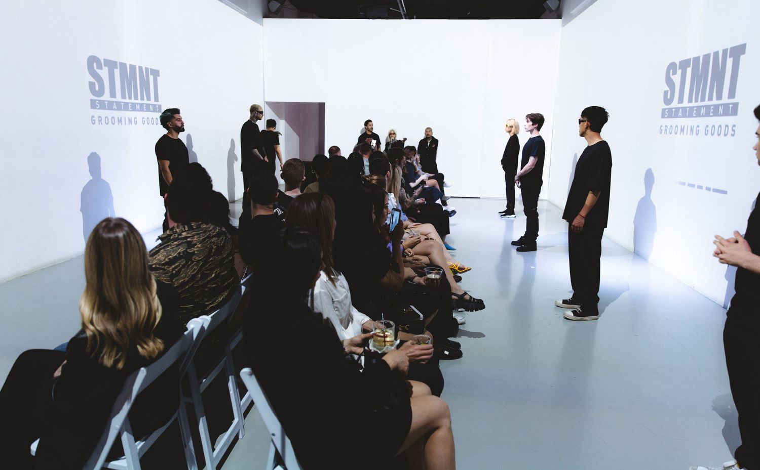 Group presentation in white minimalist space with audience seated on floor.