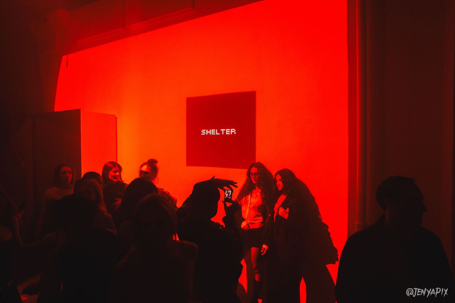 Silhouetted crowd gathering under red lighting with SHELTER branding visible.