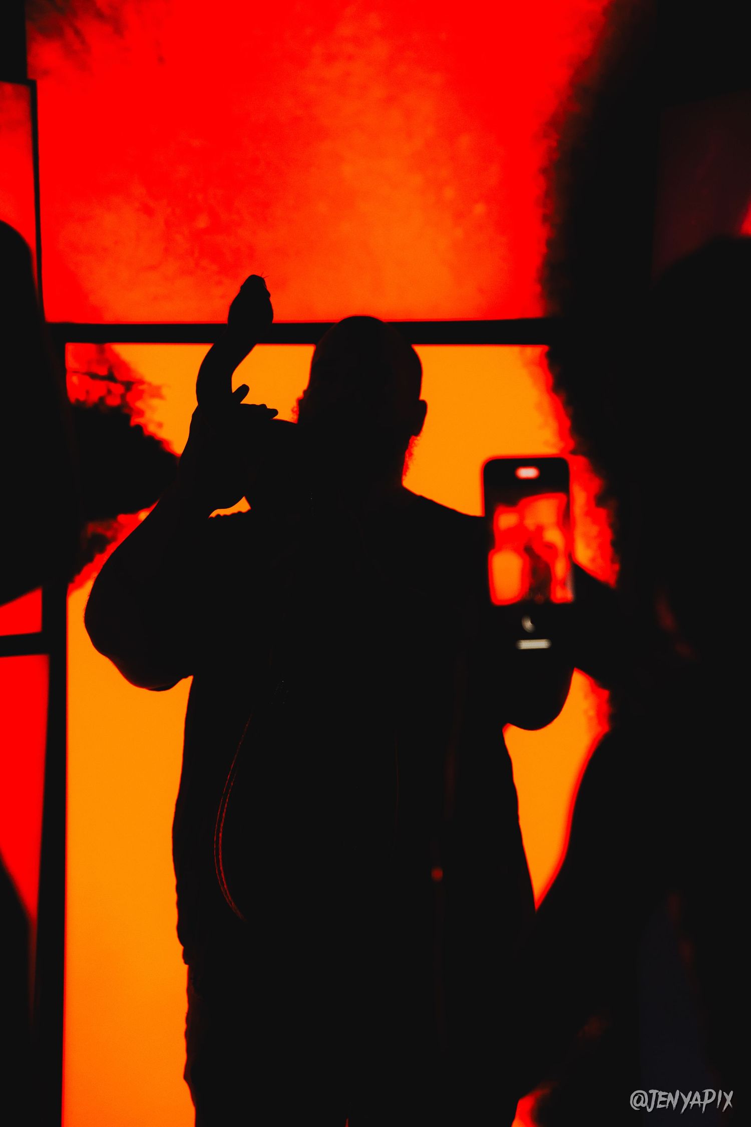 Silhouetted figures against a vibrant red-orange background at a club event.