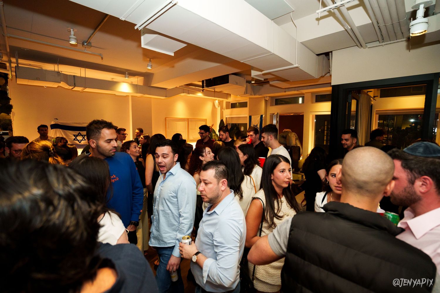 Crowded indoor networking event with young professionals mingling in a brightly lit space.