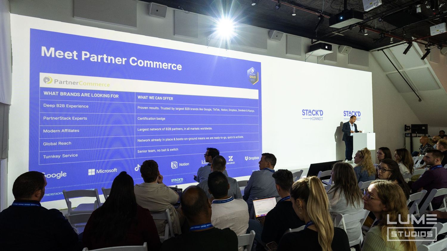 Conference attendees viewing Meet Partner Commerce presentation slide in dimly lit venue.