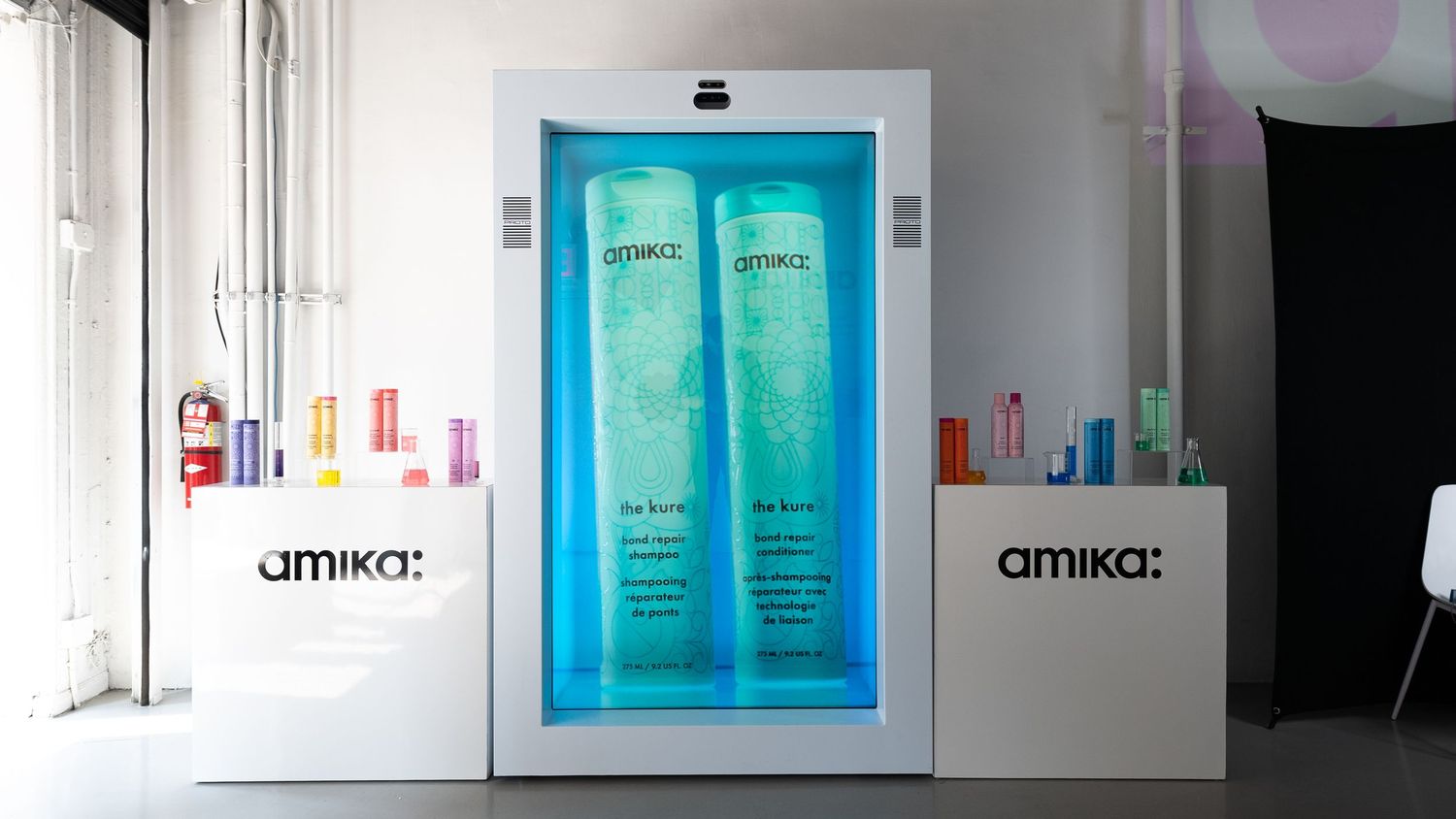 Amika branded display featuring blue beauty products and white company logos.