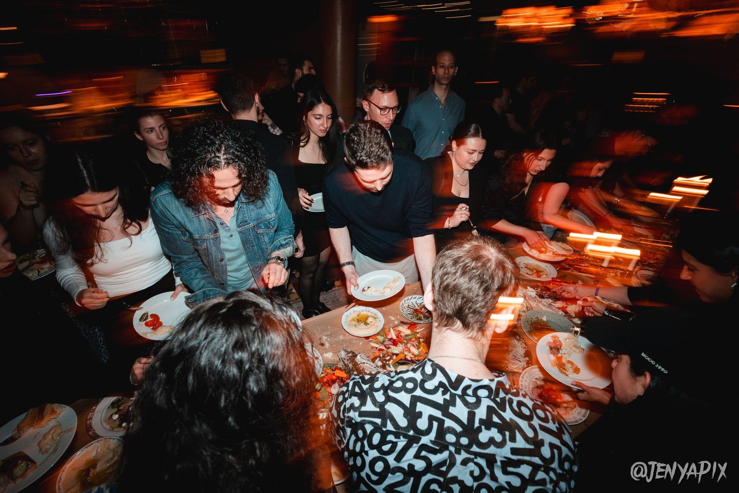 Guests enjoying dinner around a communal table at a dimly lit event.