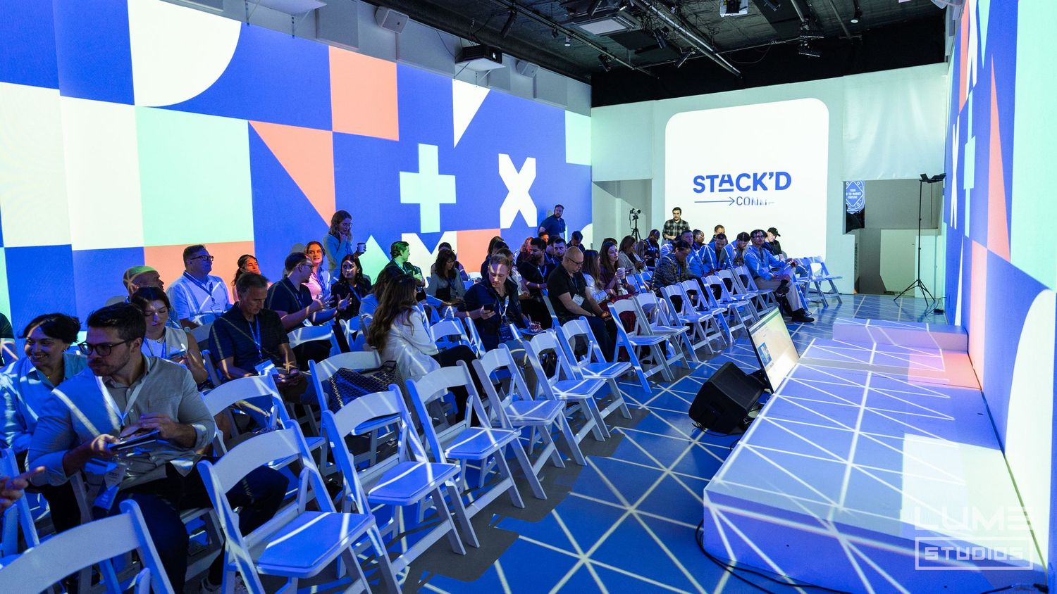 Conference setup with rows of white chairs against geometric blue and white backdrop.