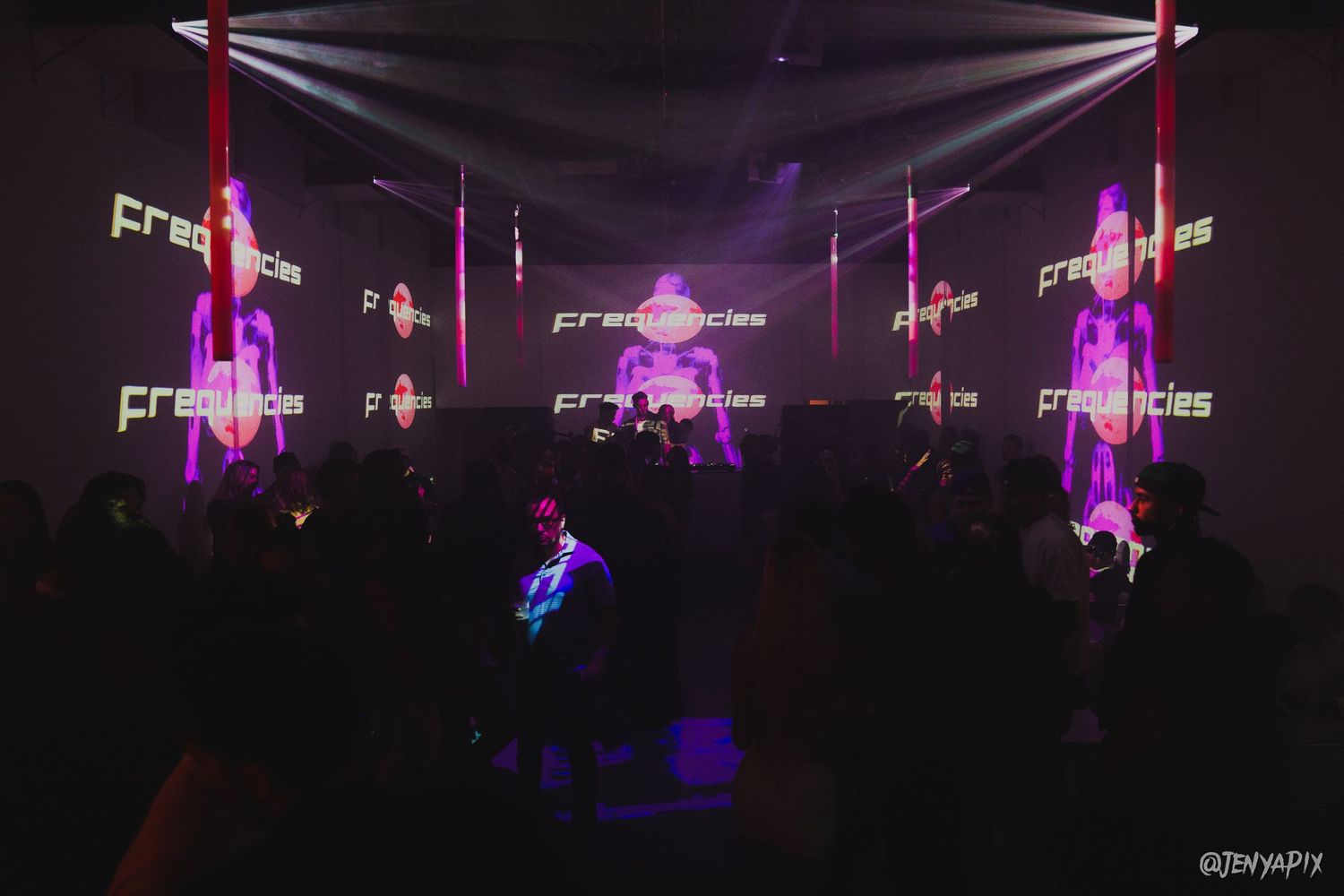 Dark concert venue with multiple projection screens displaying neon visuals.