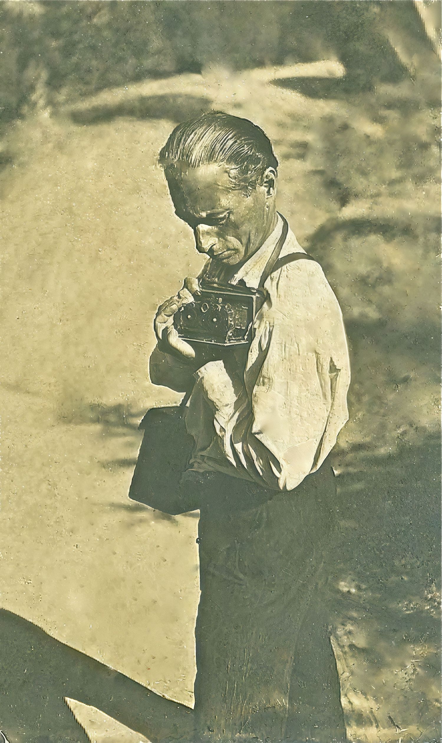 Historical black and white photo of man looking down at vintage camera.