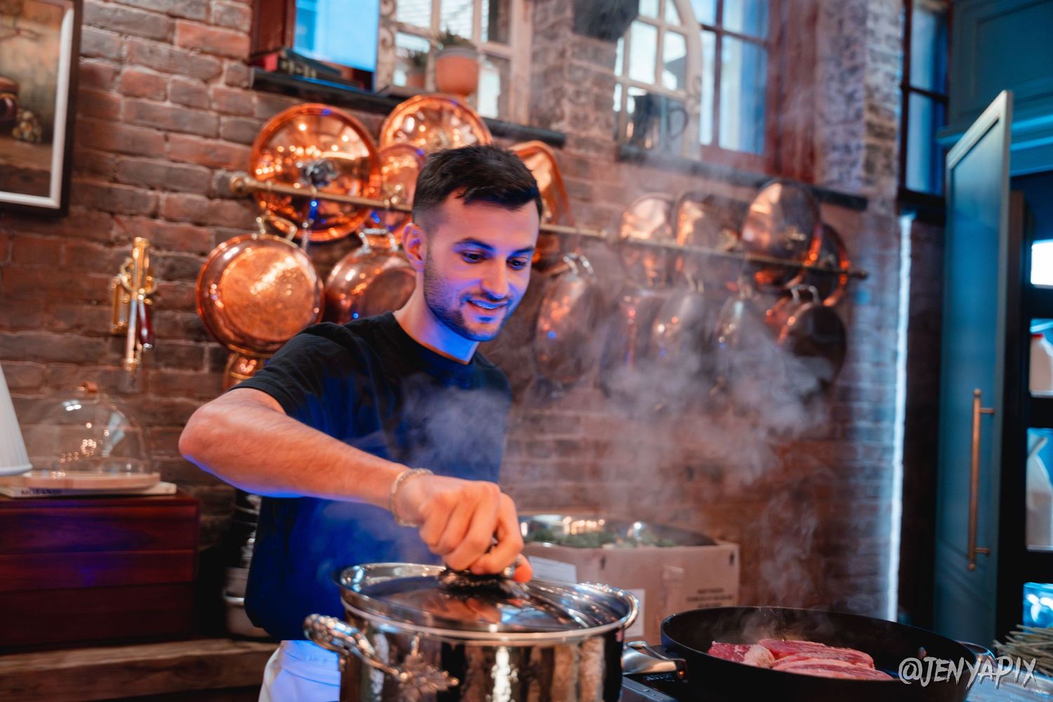 Chef cooking with steam rising from pot in rustic brick-walled kitchen.