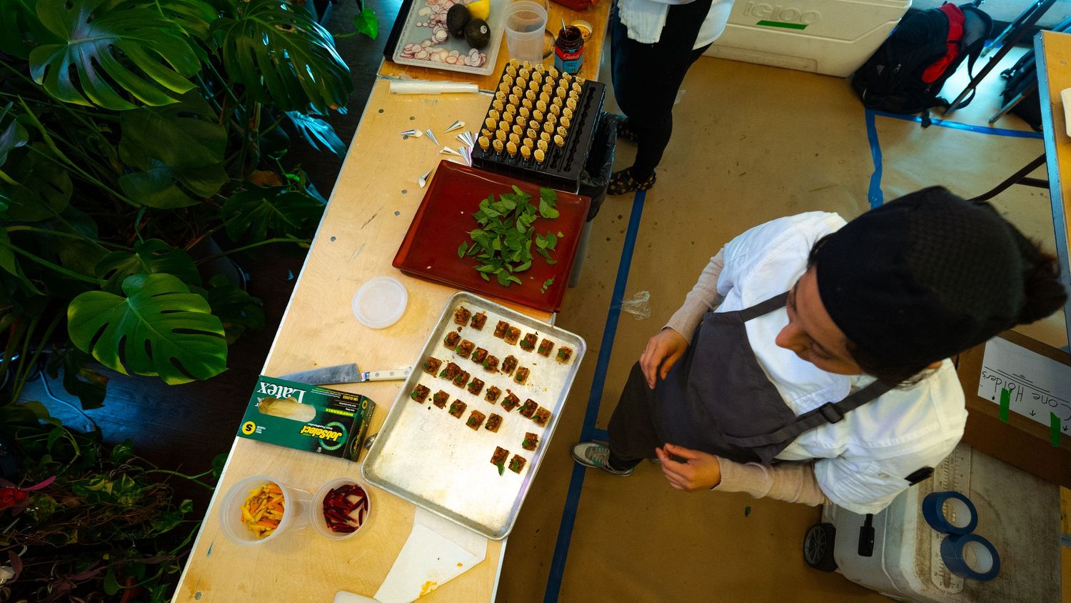 Chef preparing ingredients at wooden prep station surrounded by green plants.