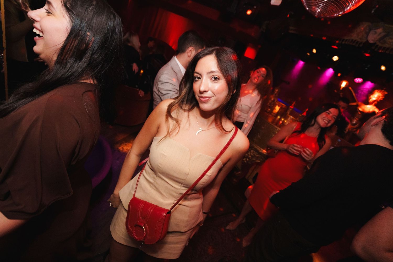 Crowded nightclub dance floor with red ambient lighting and disco effects.