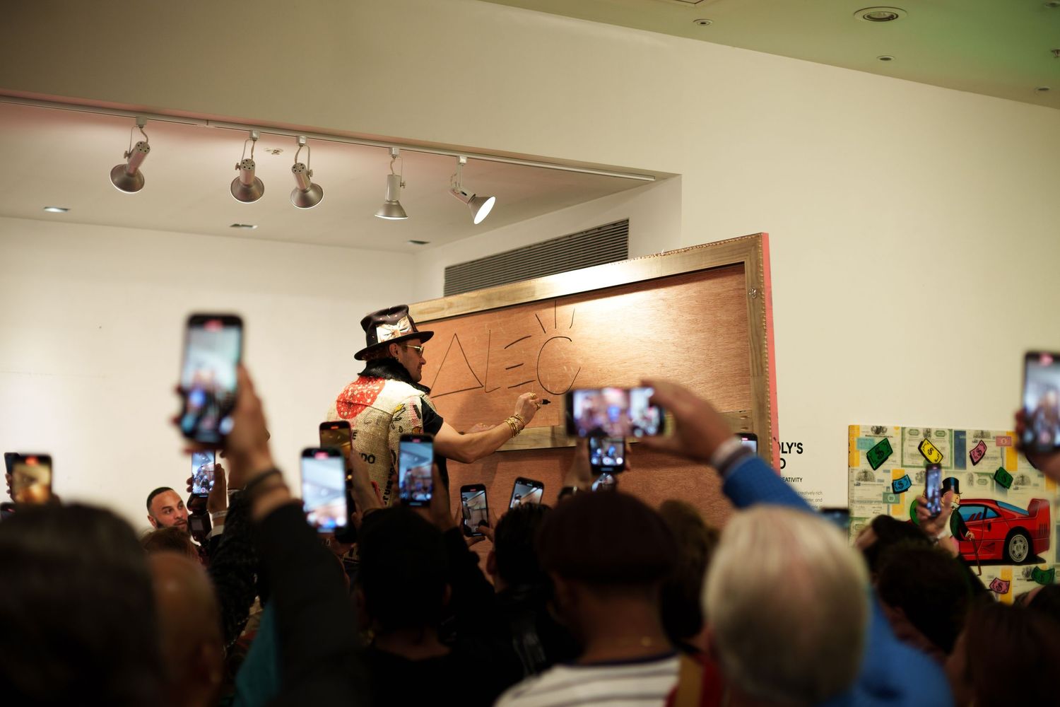 Crowded art gallery event with spotlights illuminating artwork on wooden walls.
