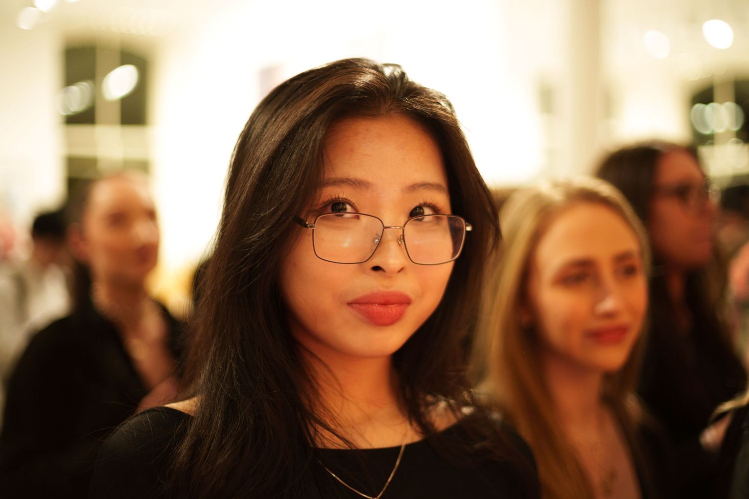 Candid portrait of gallery attendee wearing glasses at evening art event.